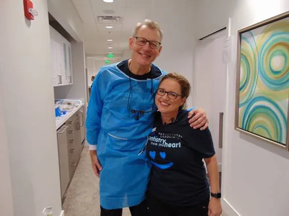 Two dental professionals in blue medical scrubs posing in hallway with abstract artwork on wall