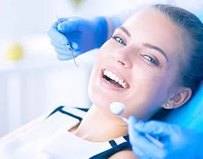 Female patient receiving dental treatment, lying back in dental chair while dentist in blue gloves examines her teeth